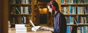 Man with headphones working on laptop in library | The Career Academy Ireland