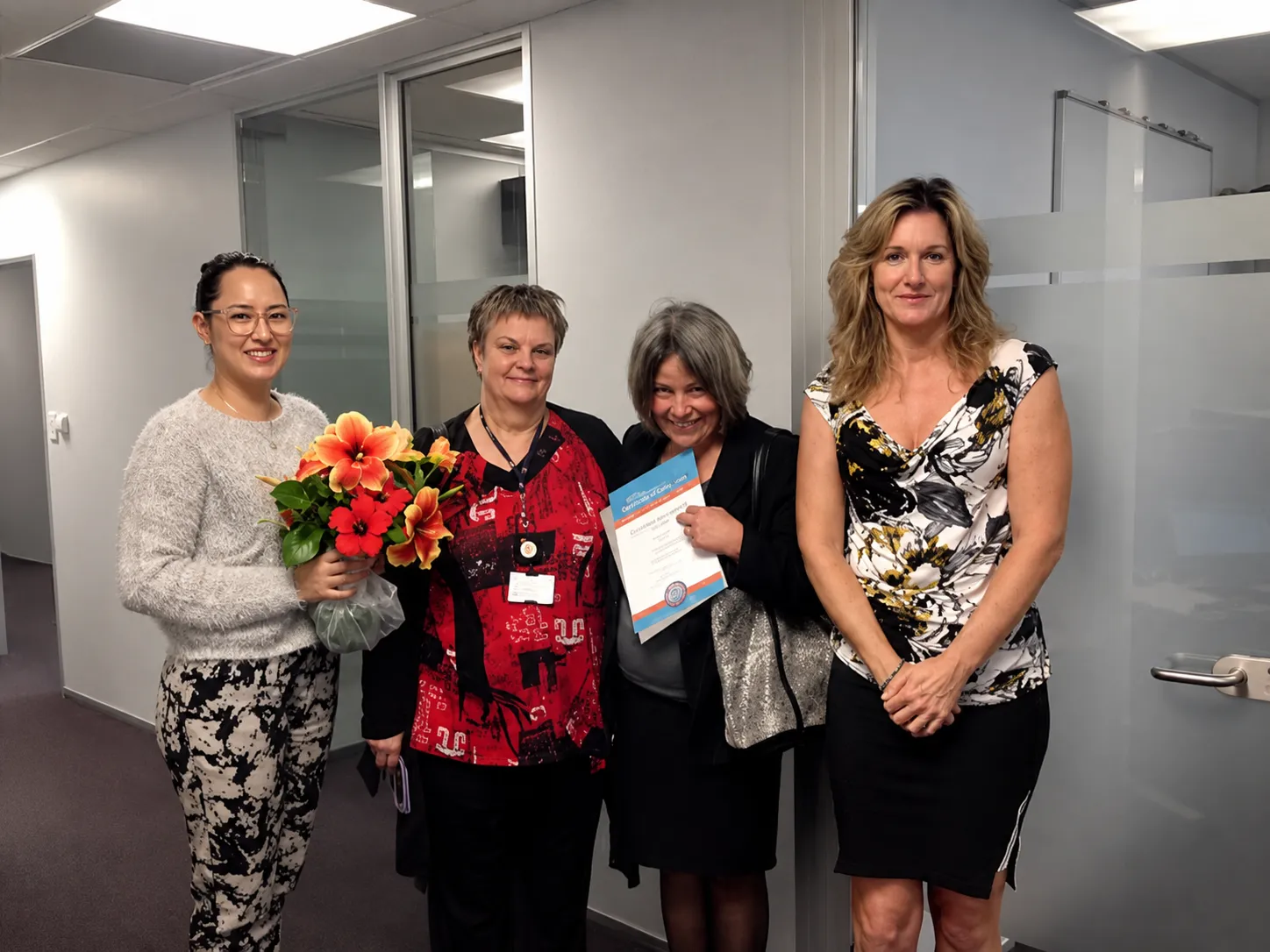 Four women celebrating a certificate presentation in an office